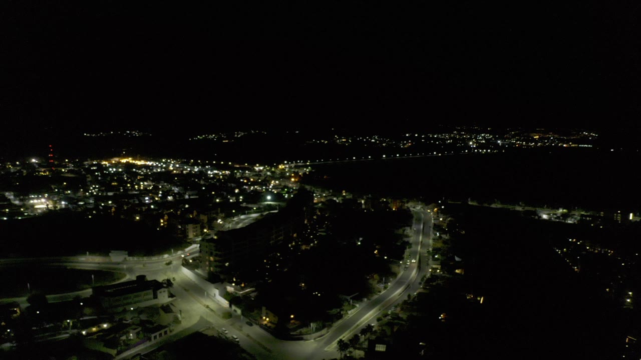Night aerial view of lit streets and dark buildings near water.