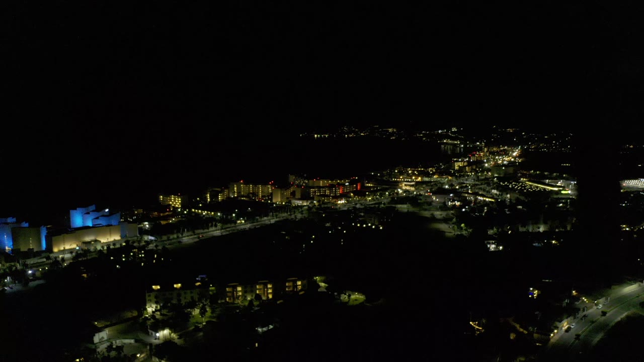 Dark aerial city edge with lit buildings and curving roads at night.