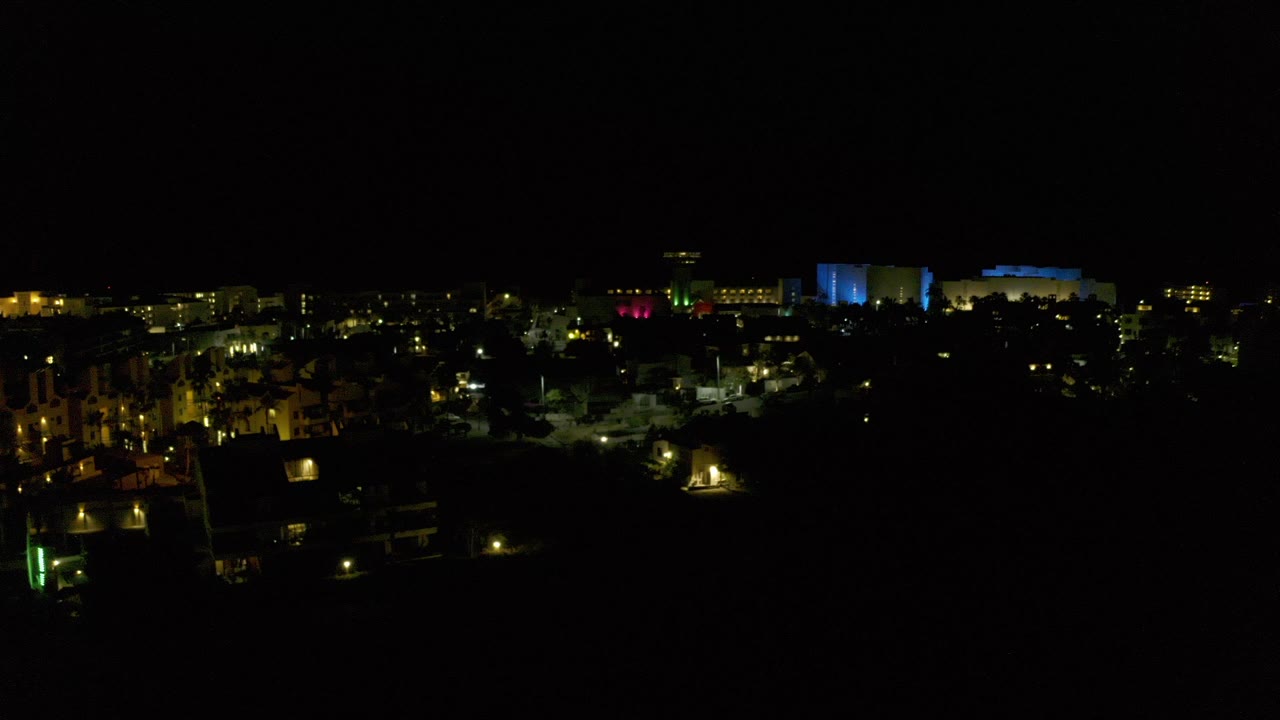 Wide nighttime view over Los Cabos, Mexico, with scattered warm lights, dark tree silhouettes, and no visible people.