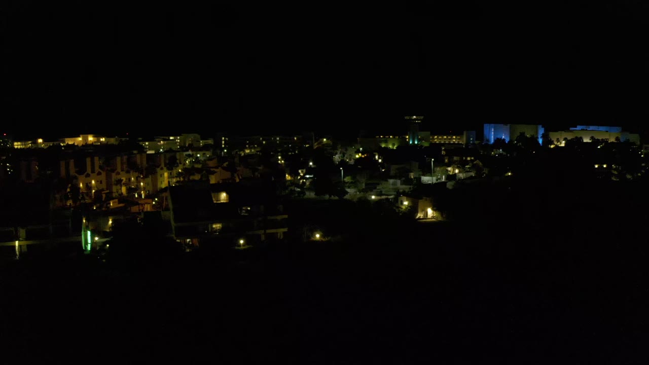 Los Cabos night scene with a band of lit homes and buildings across the lower image, a mostly black sky, and no visible people.