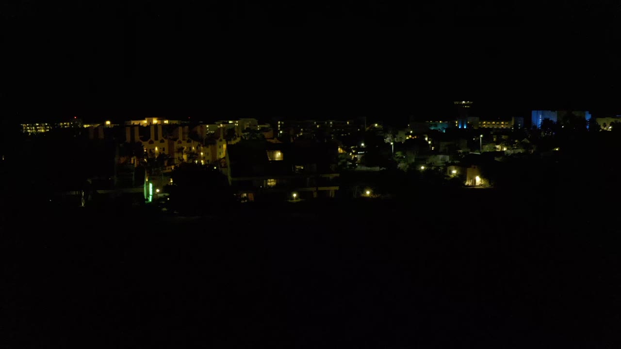 Los Cabos night frame with a mostly black sky, tiny background lights, a green vertical light near the lower left area, and no visible people.