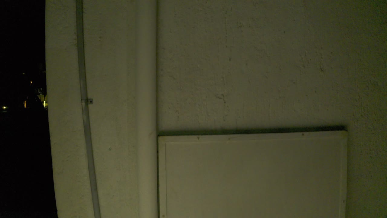Dim white wall or door with a vertical rod and dark gaps at the sides.