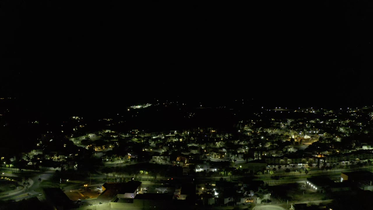 Los Cabos city lights continue across the lower half of the frame, with brighter street lamps near the foreground and no visible people.