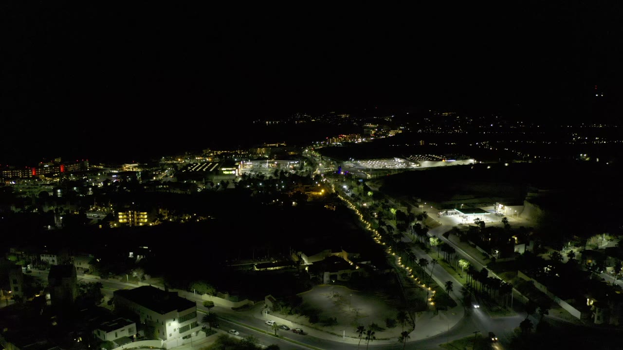 Night drone view over a city grid with bright roads and dark open areas.
