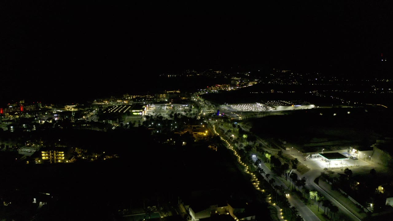 Wide nighttime view over Los Cabos, Mexico, with a dark foreground, lit roads, clusters of buildings, and no visible people.