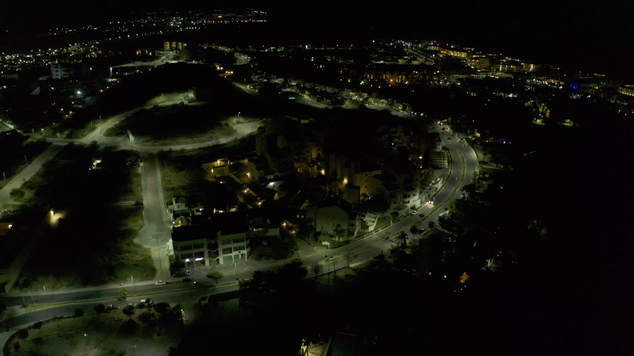 Night aerial view of lit roads and buildings beside dark open ground.