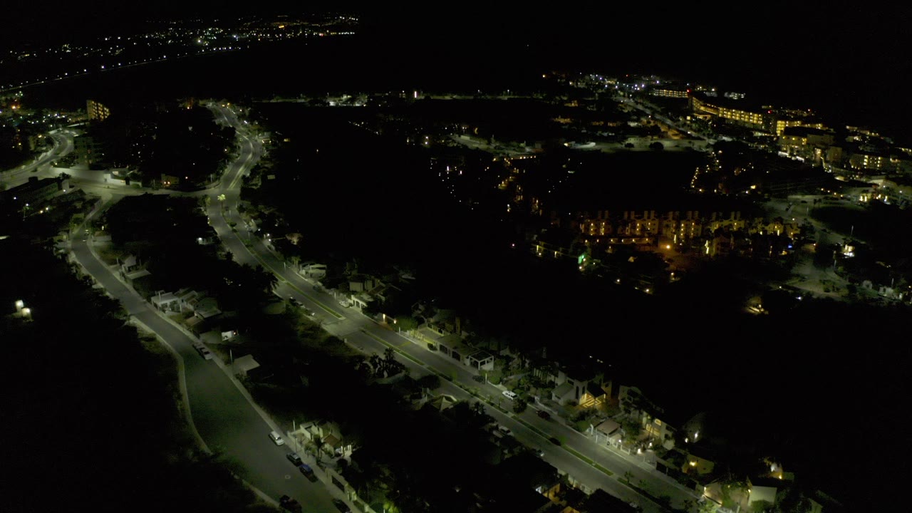 Opening aerial frame over Los Cabos at night, with curving roads, scattered streetlights, distant building lights, and no visible people.
