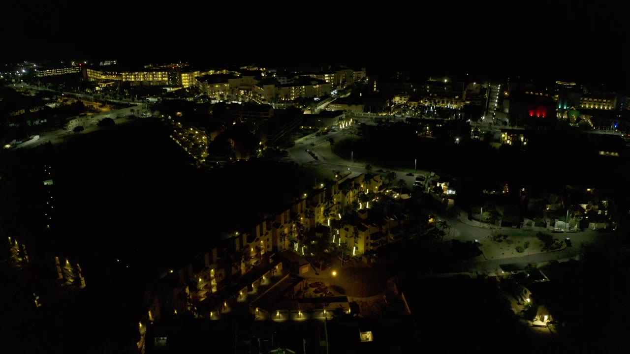 Second nighttime frame over Los Cabos with the brighter building line held near the top, smaller lit streets below, and no visible people.