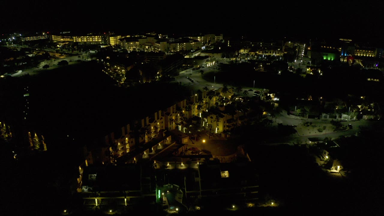 Night aerial view of lit buildings and roads in a dark landscape.
