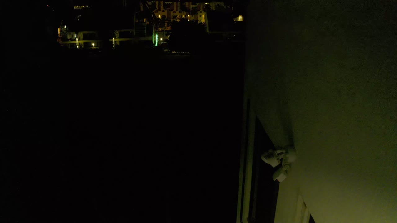 At 0:01, the Los Cabos night frame remains mostly black, with warm architectural lights at the upper edge and the pale wall or column holding the right side of the composition.