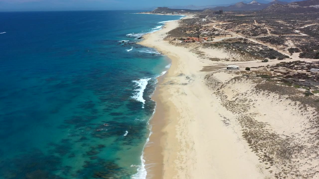 Blue ocean and pale beach curve along scrubby coastal land.
