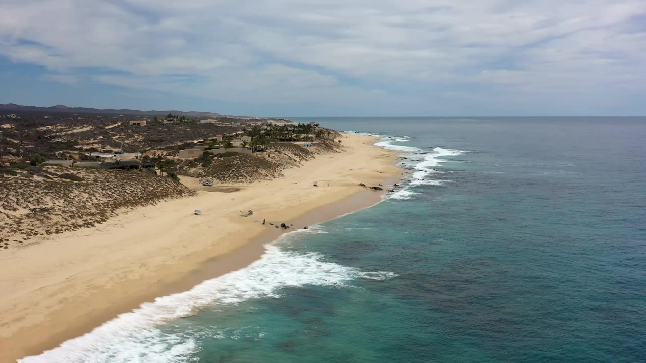 Aerial view of sandy beach, surf, dunes, and blue ocean.