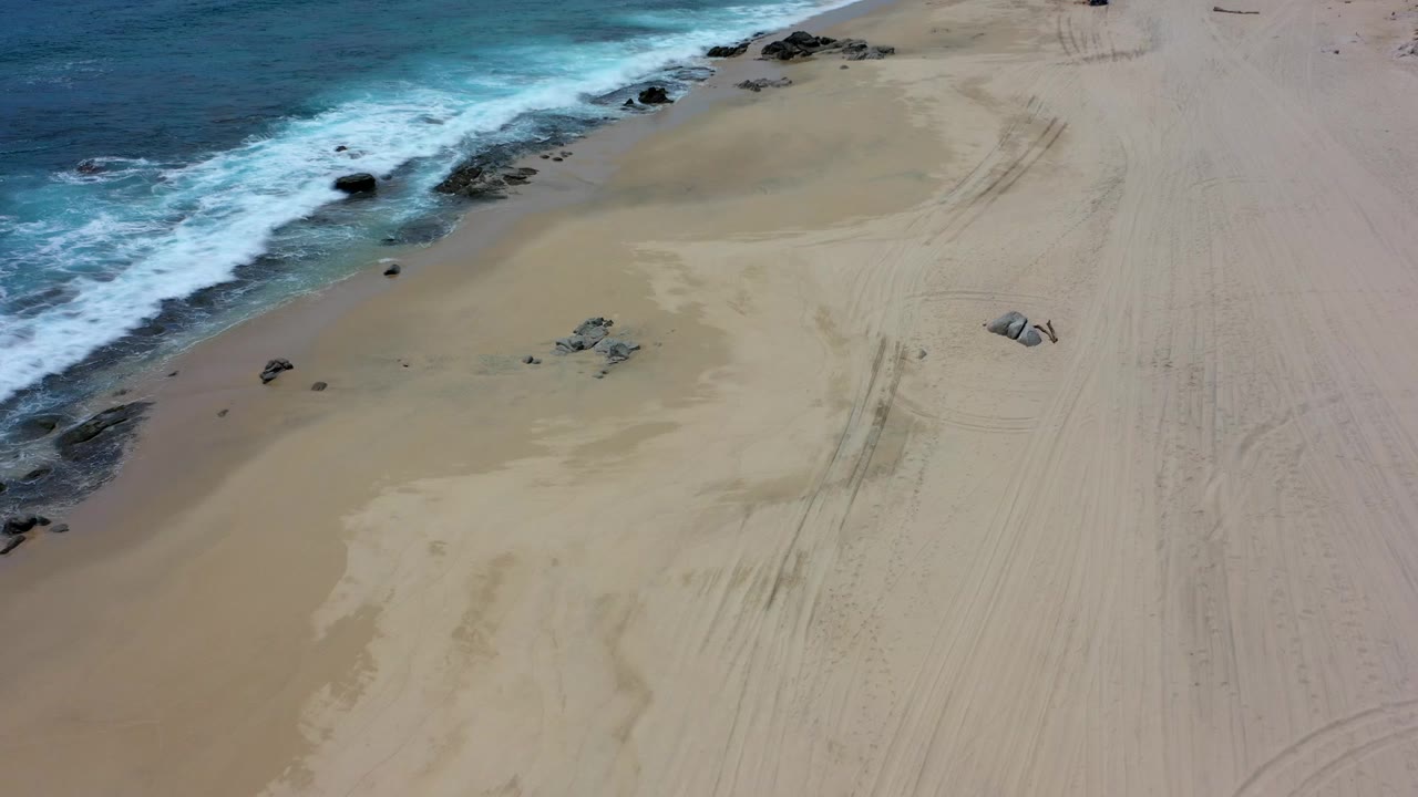 Overhead view of waves reaching a sandy beach with rocks near shore.
