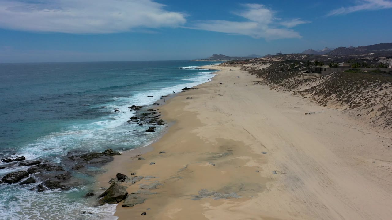 Aerial view of a sandy beach beside blue ocean surf.