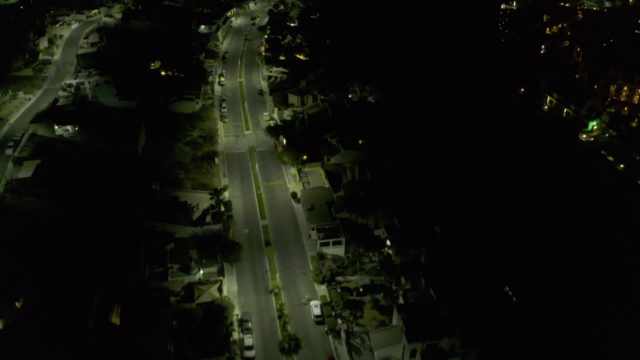 Night aerial view of a lit road beside dark buildings and trees.