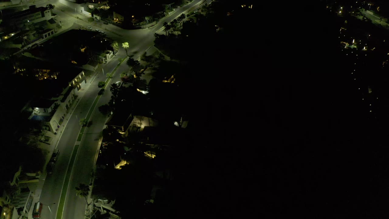 A high nighttime view in Los Cabos, Mexico shows the road stretching diagonally under greenish streetlights, with no visible people.
