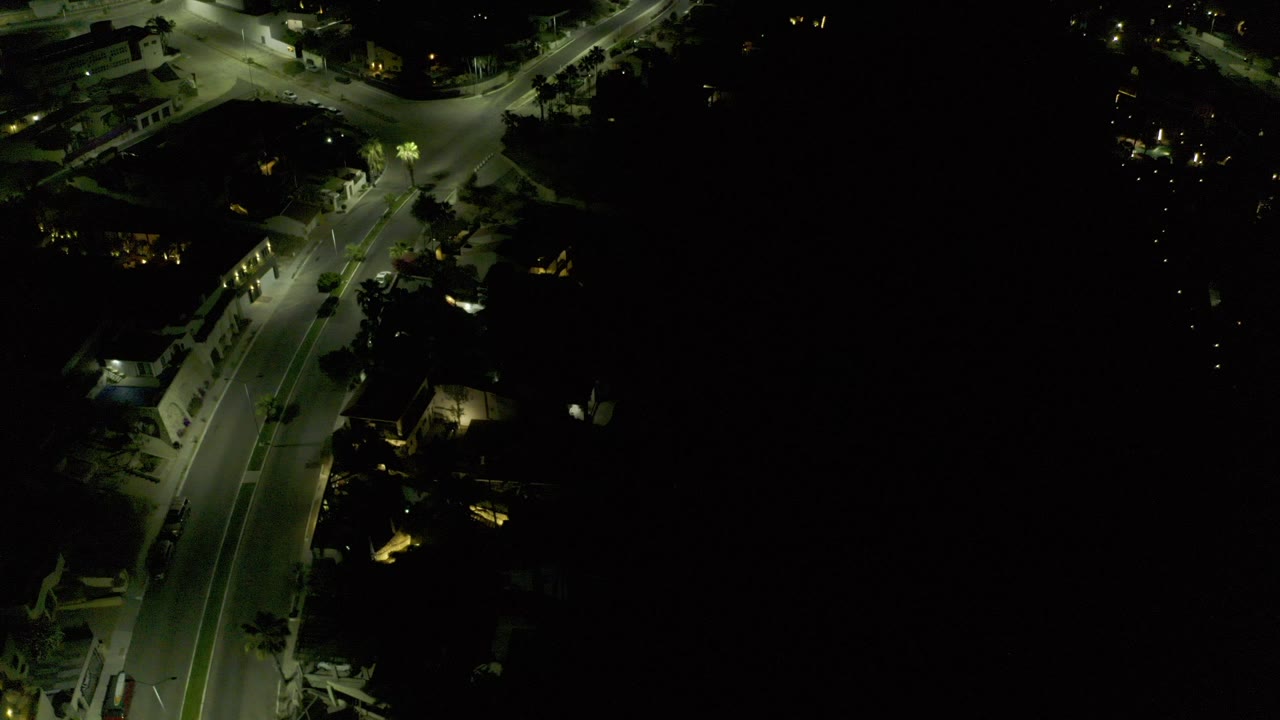 A high night view over Los Cabos, Mexico shows curved roads, small pools of streetlight, dark building areas, and no visible people.