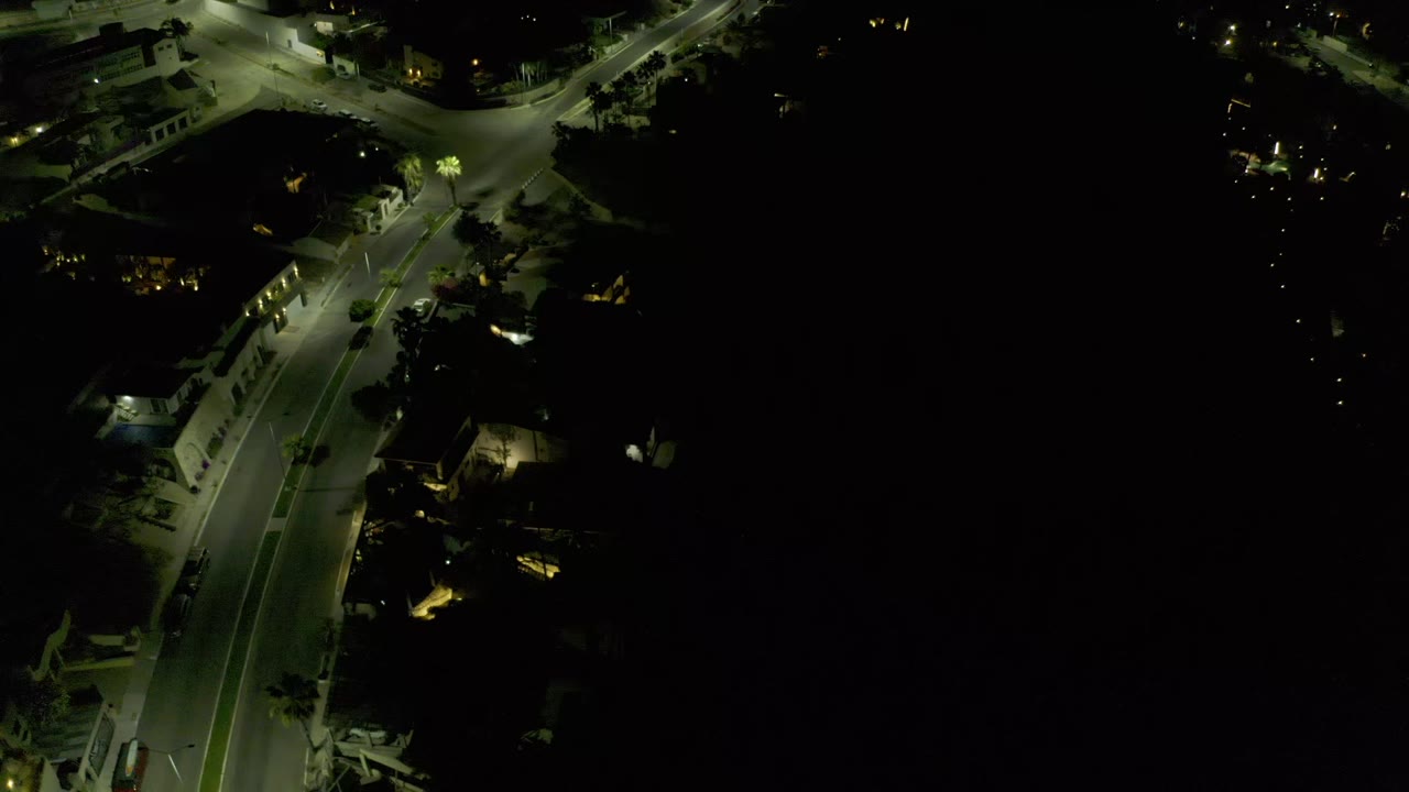 An overhead frame in Los Cabos, Mexico centers on a lit road junction with dim buildings around it and no visible people.