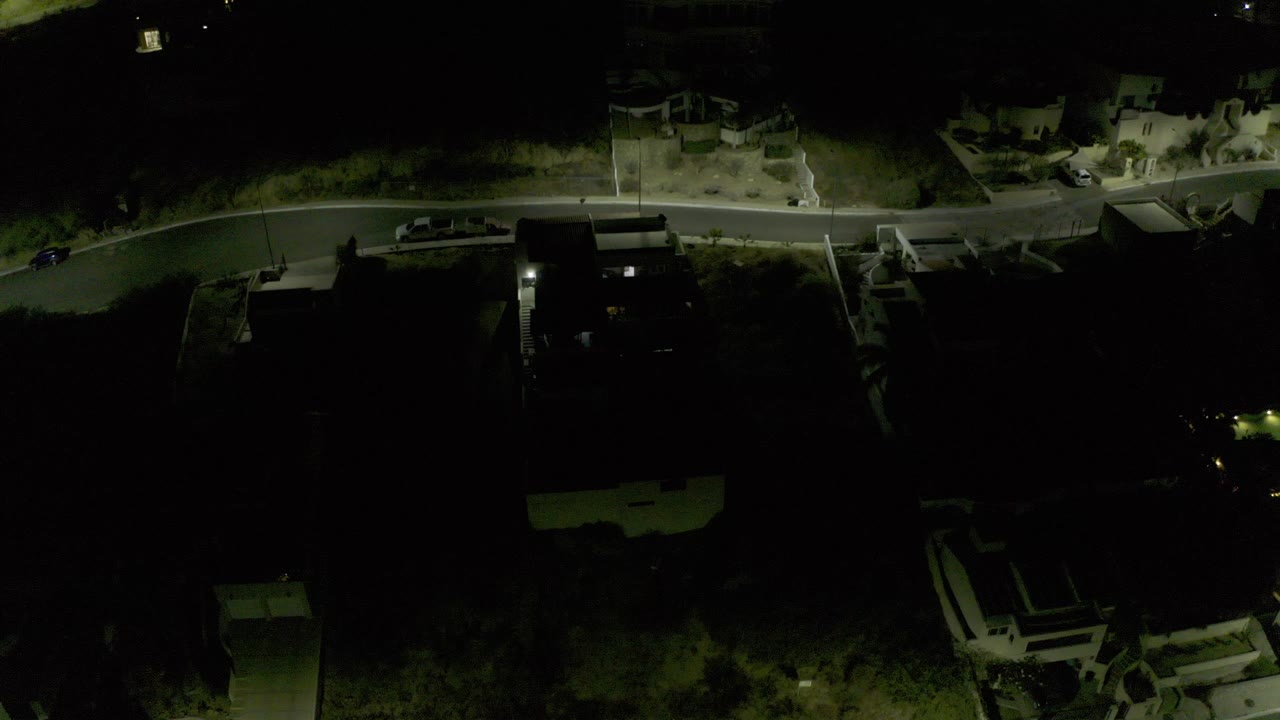 Overhead night view of a curved road beside dark condominium buildings and trees.
