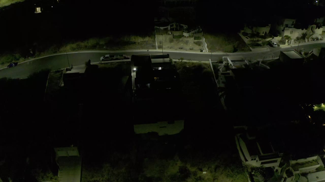 Second frame over Los Cabos, Mexico, with the lit road running across the upper frame, condominium rooftops below, trees in shadow, and no visible people.