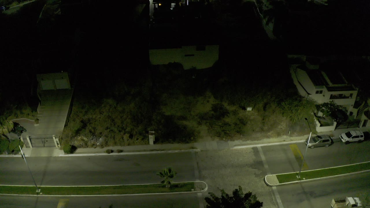 Overhead night view of a quiet street with parked cars and streetlight shadows.