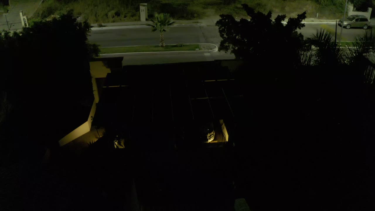 The Los Cabos home remains mostly in shadow while two small driveway lights glow below the road, with no visible people in the frame.