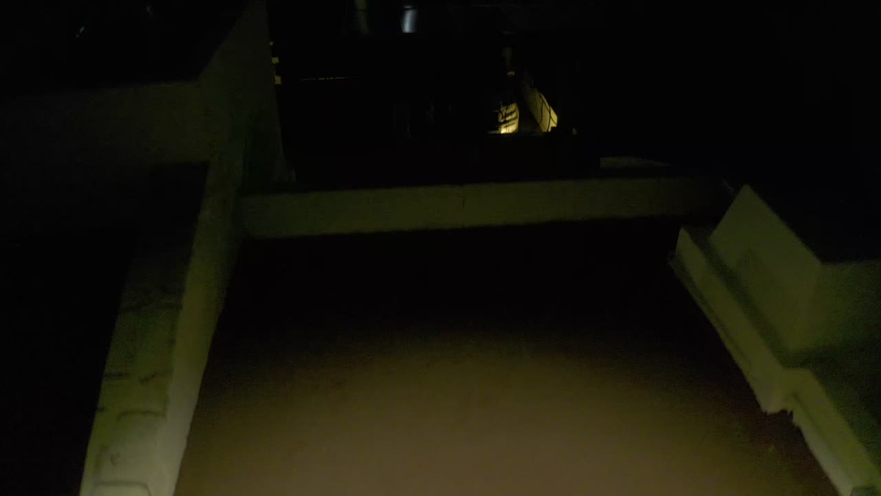 Second frame showing the rooftop foreground closer in darkness, with angular house walls, sparse lights, and no visible people.