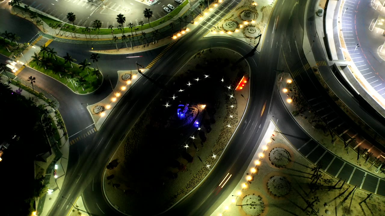 Overhead night view of a lit roundabout with car light trails.