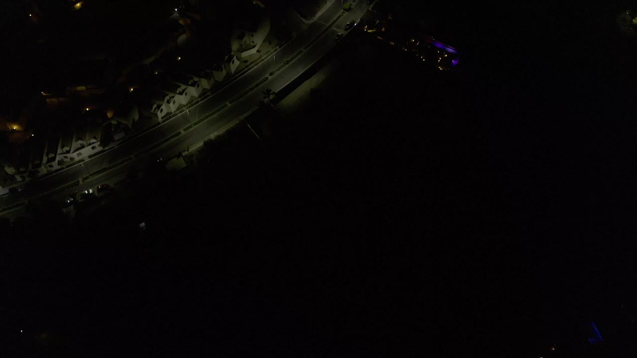 Dark aerial view over Los Cabos, Mexico with a curving street near the upper frame, scattered lamps, and no visible people.