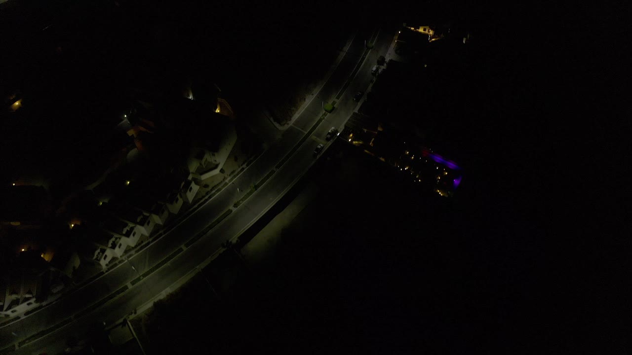 Dark aerial frame over Los Cabos, Mexico, with a curved road crossing the left side, scattered building lights, and no visible people.