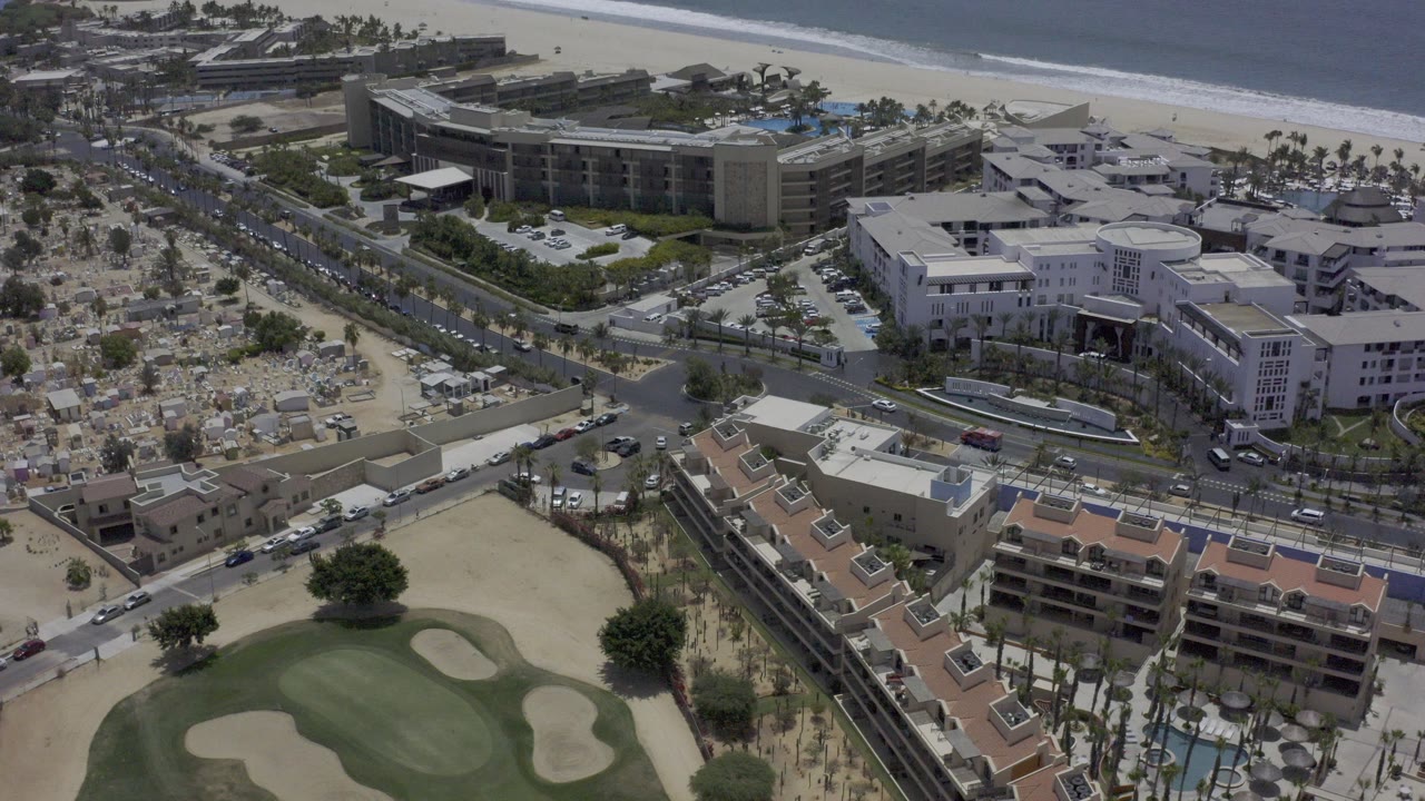 Aerial view of a golf course beside roads, buildings, beach, and ocean.
