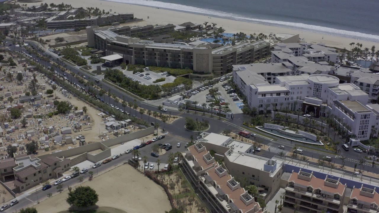 Drone-style view of coastal hotels, streets, parking, and beach.