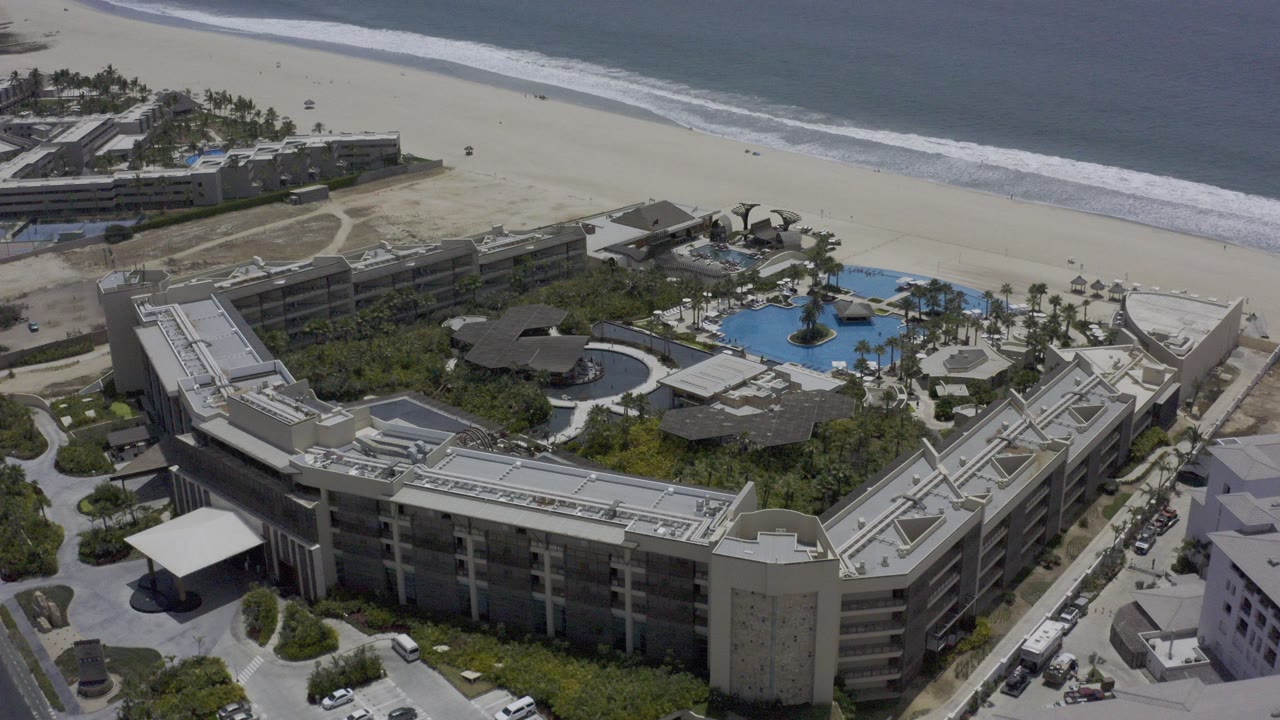 Aerial view of a beachfront resort with pools, hotel buildings, beach, and ocean.