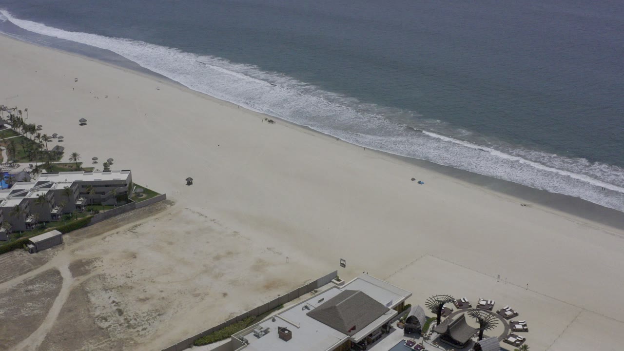 Aerial view of sandy beach, surf, ocean, and beachfront houses.