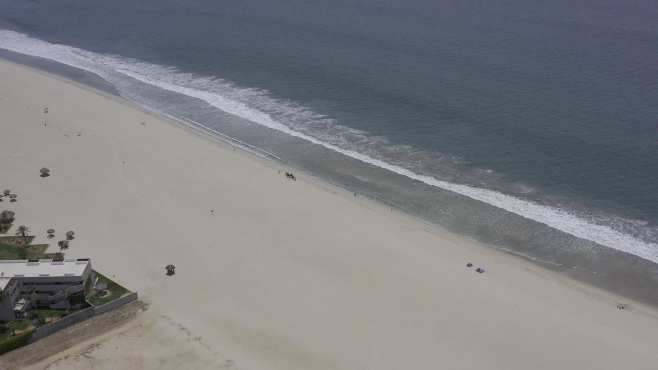 Aerial view of waves reaching a wide sandy beach.