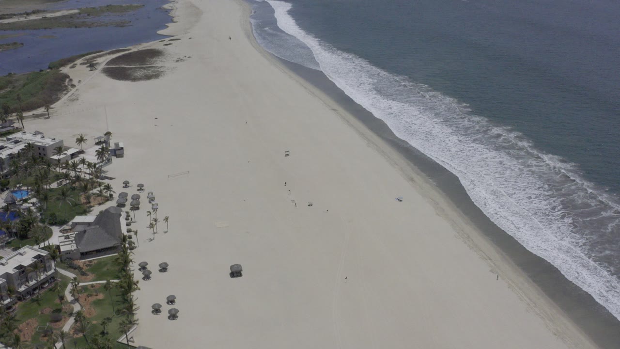 High aerial view of pale beach, surf, wetlands, and shoreline houses.