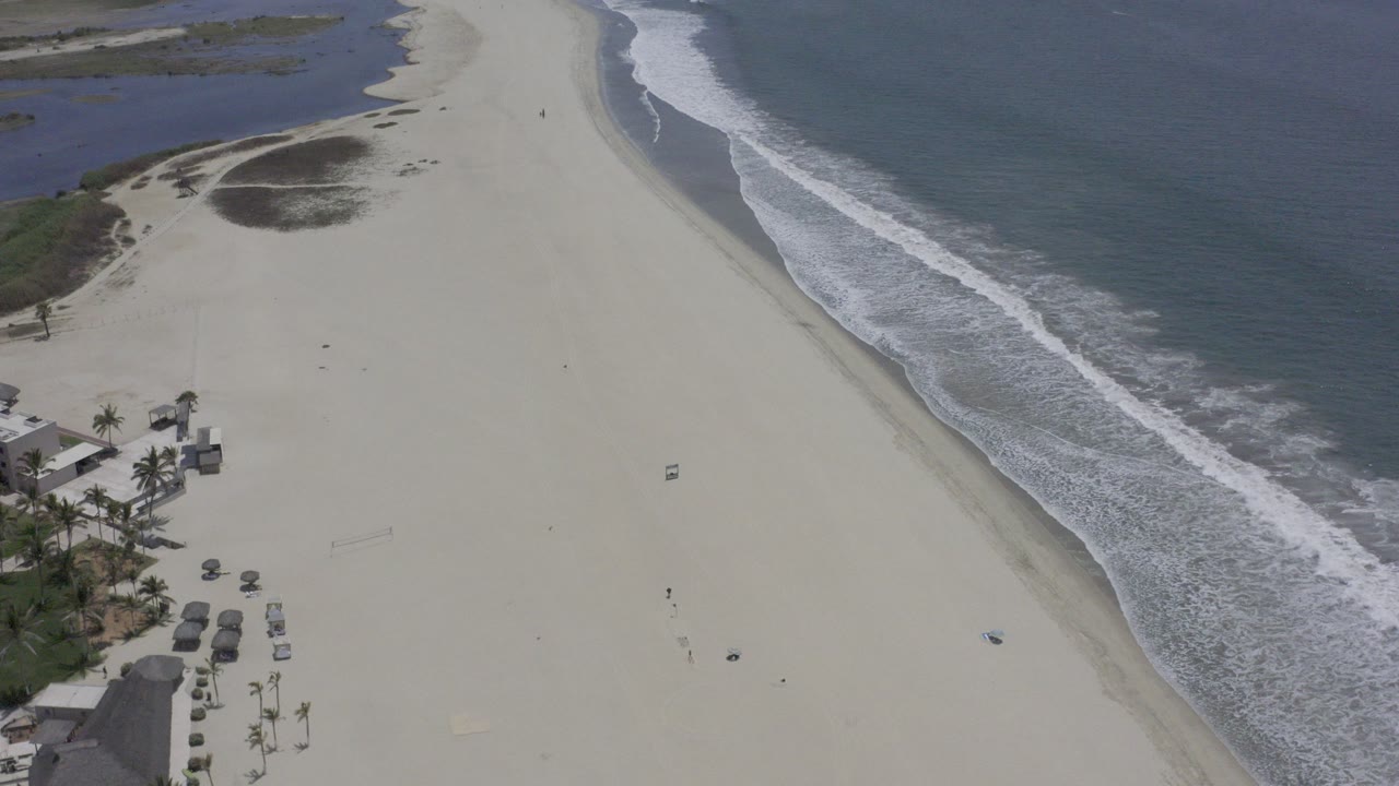 Aerial view of a sandy beach with ocean waves and palm-side beach structures.