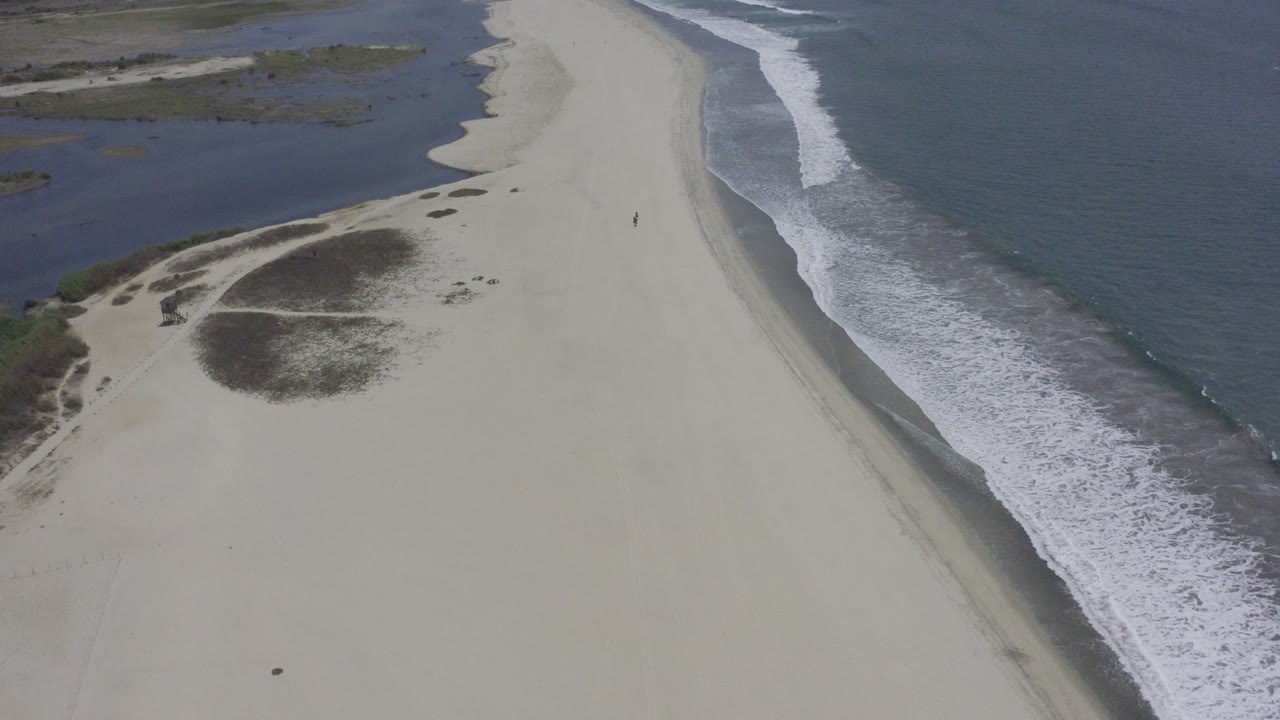 Wide aerial beach view with water on both sides of the sand.