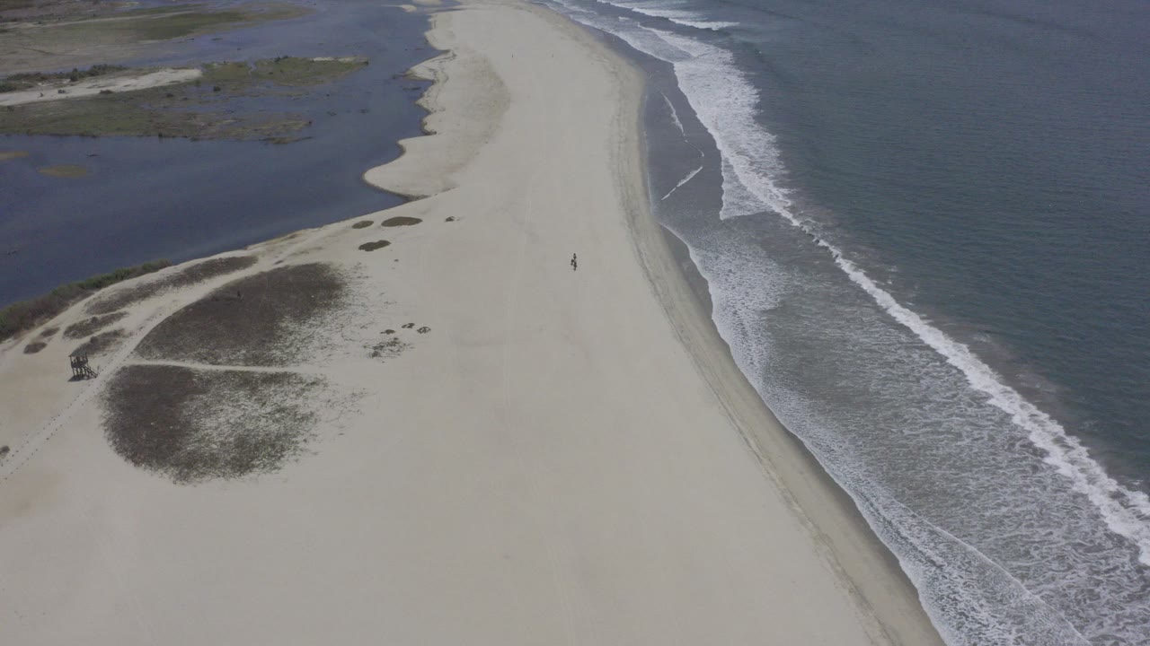 Overhead Los Cabos beach frame with pale sand between dark lagoon water and blue ocean surf, no visible people.