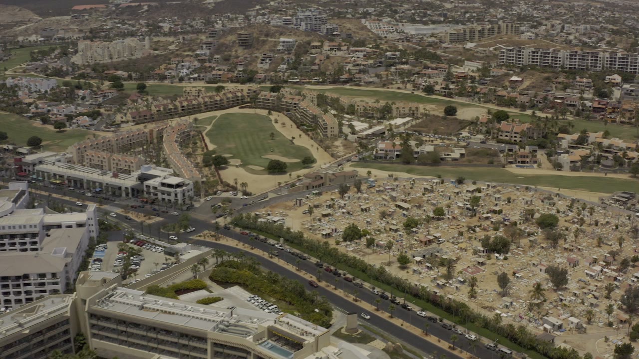 Drone-height view across urban outskirts with a cemetery-like area and sports field.