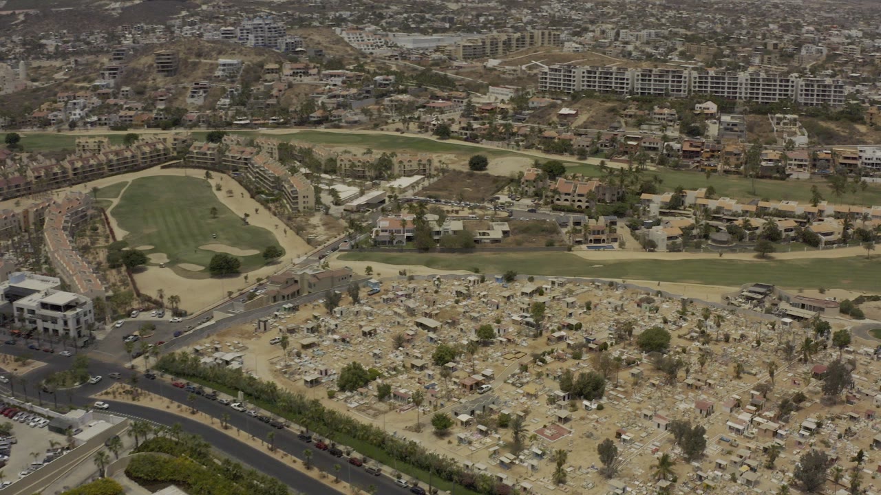 Aerial view of dry marker-filled land beside roads, green fairway, and hillside housing.
