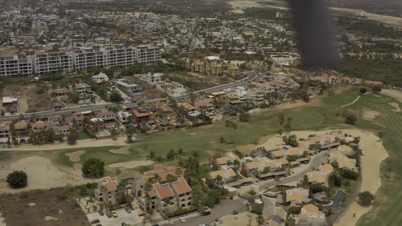 Aerial view over homes, golf-course greens, and hillside buildings.