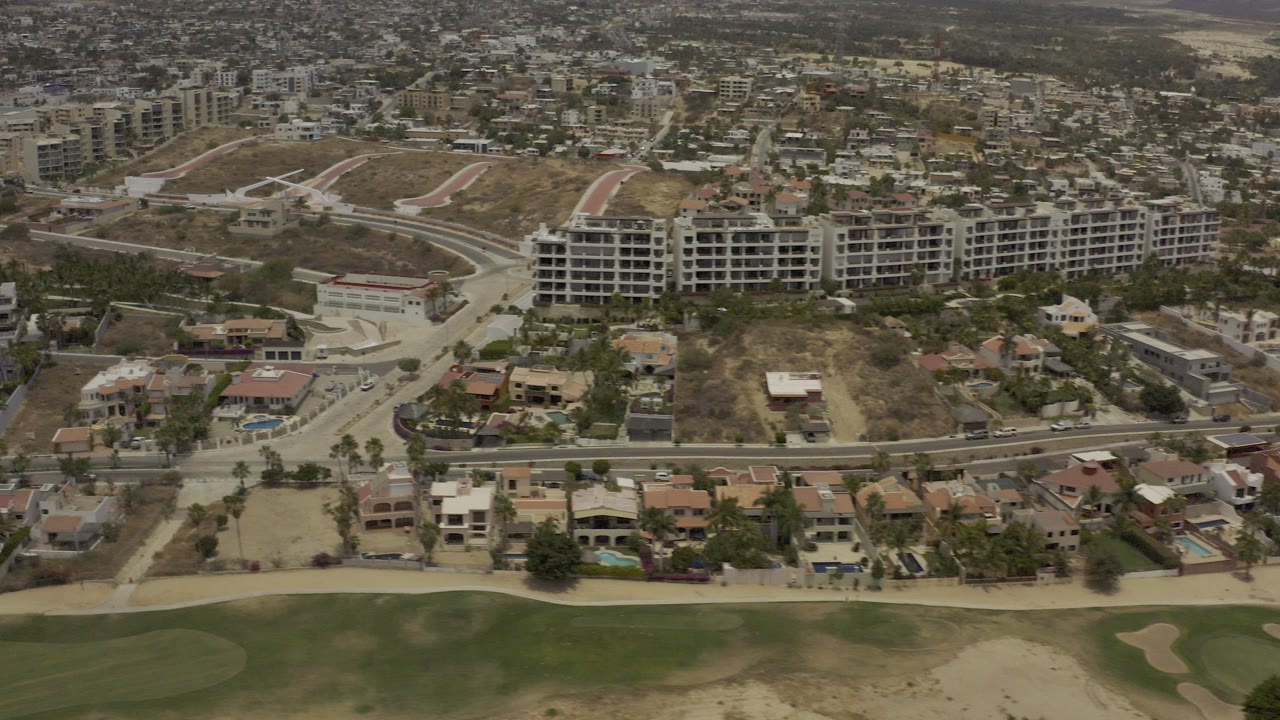Aerial view of houses, roads, dry hills, and green golf course edge.