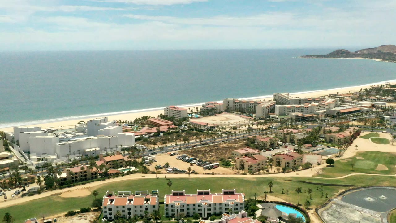 Aerial view of beachfront buildings, golf course, beach, and ocean.