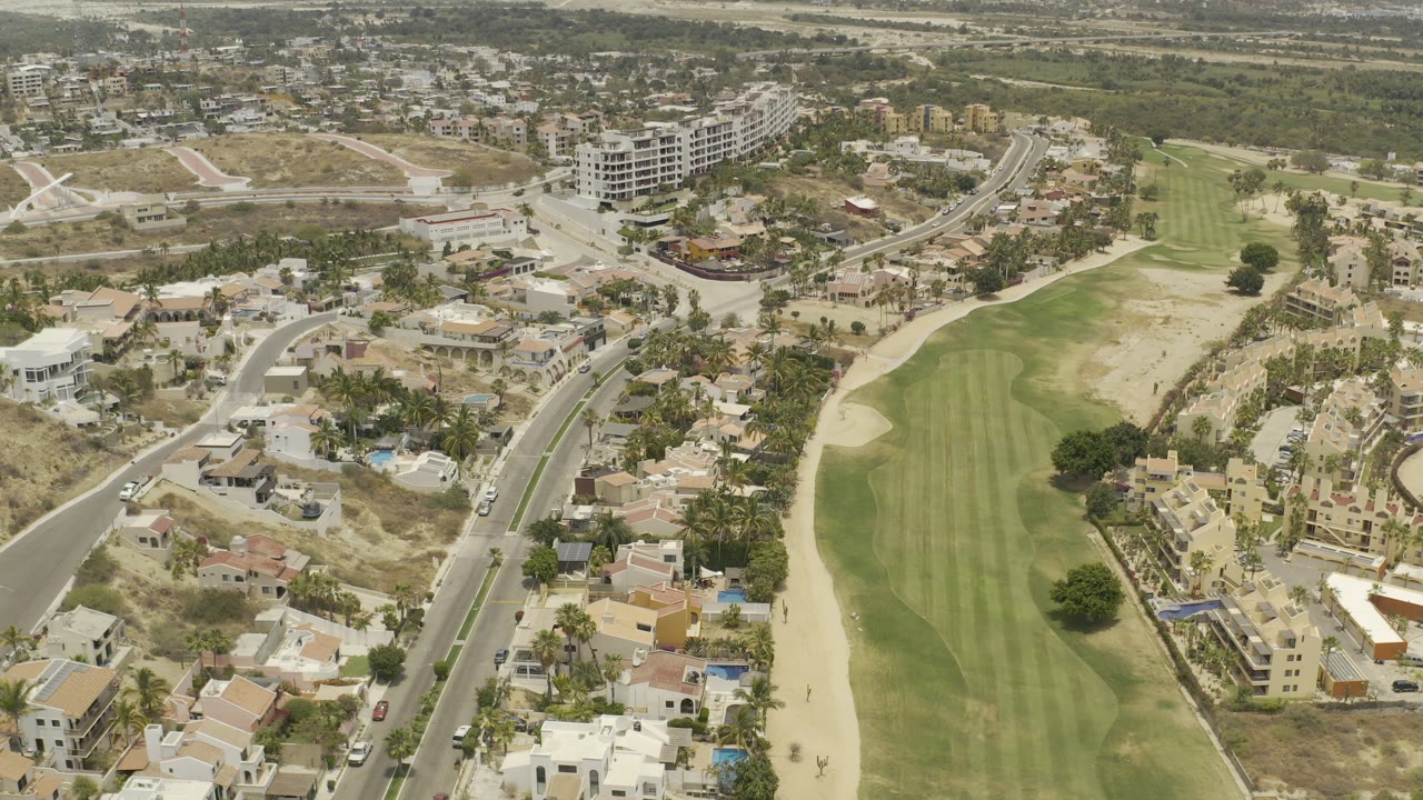 Aerial view of homes, roads, and a green golf fairway beside dry land.