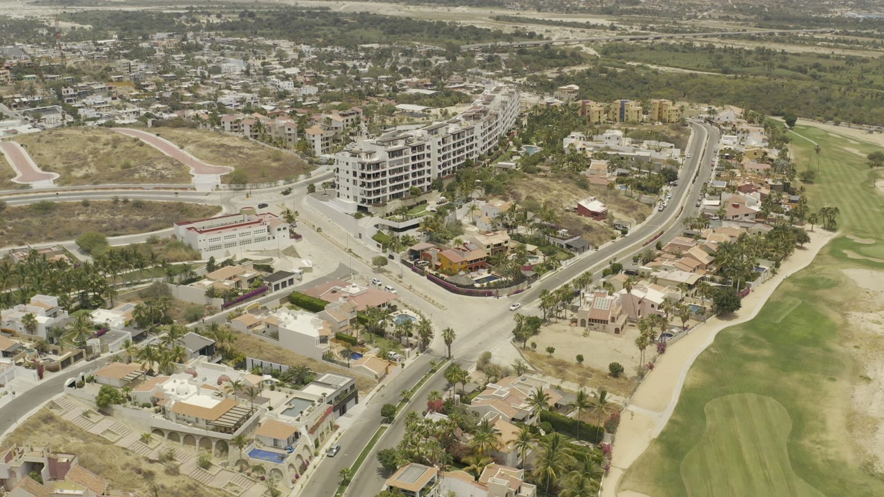 Aerial view of roads, homes, hotel building, dry land, and golf-course grass.