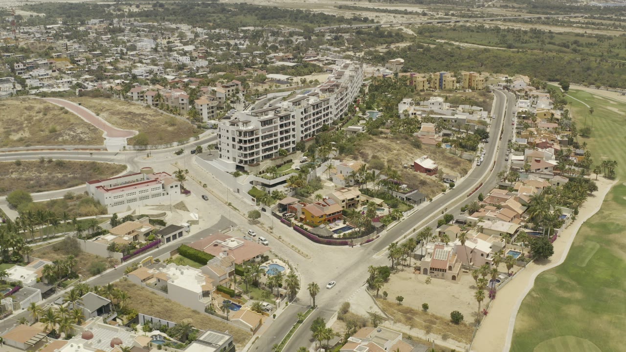 Aerial view of a road junction, homes, white buildings, and golf course greens.