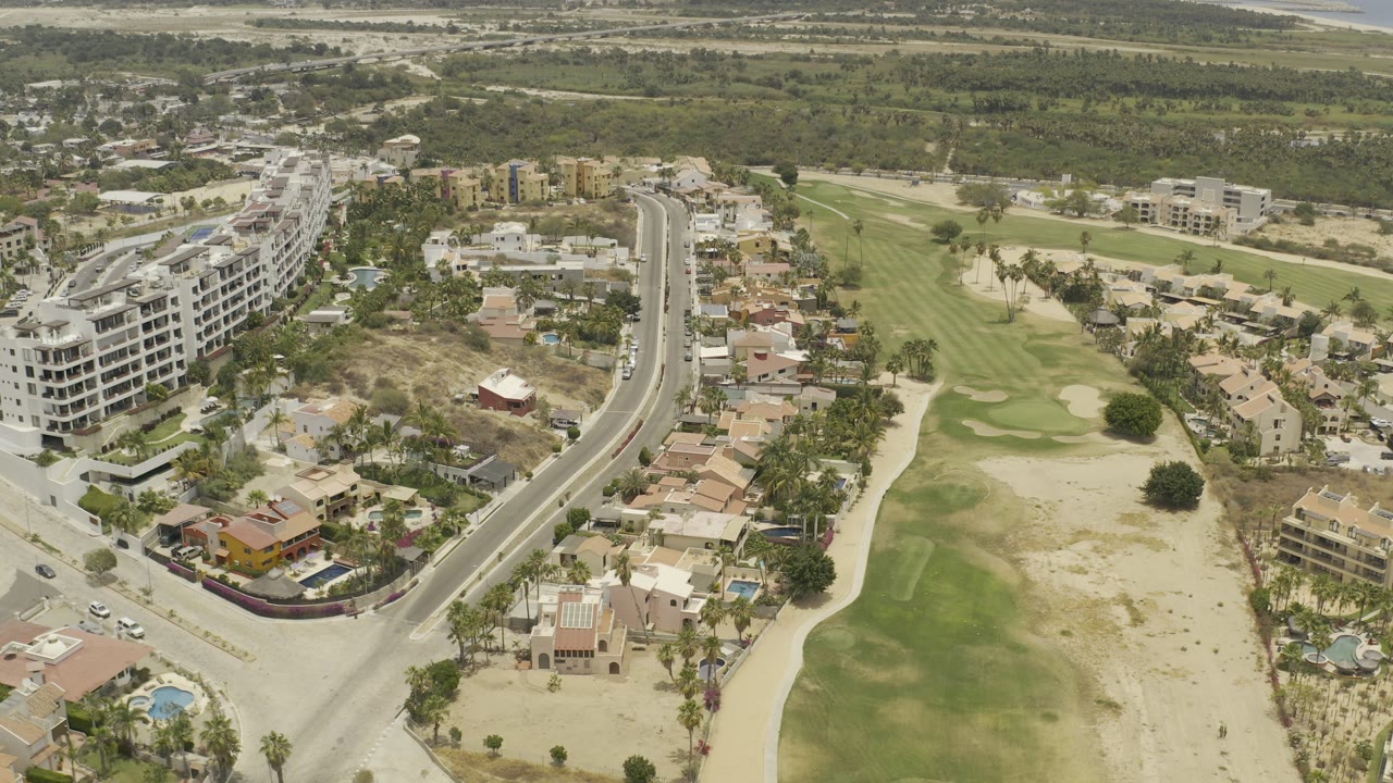Drone-like view of condos, villas, golf fairways, and dry sandy ground.