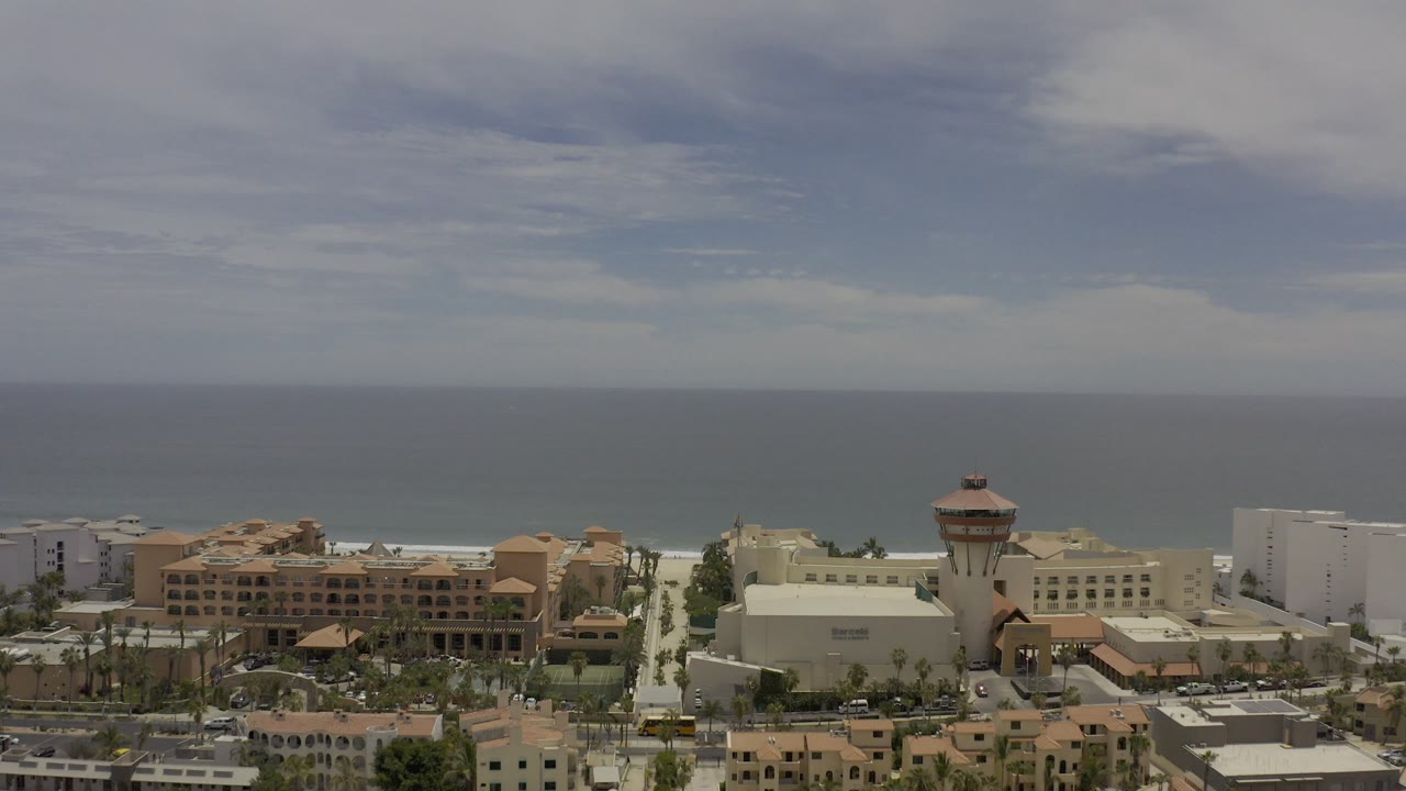 Coastal hotel buildings and palm trees below a cloudy ocean horizon.