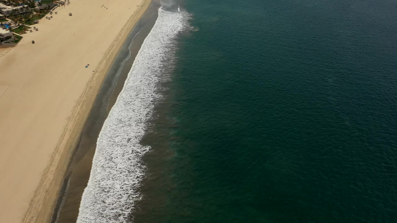 Overhead beach shoreline with sand, surf, and dark ocean water.